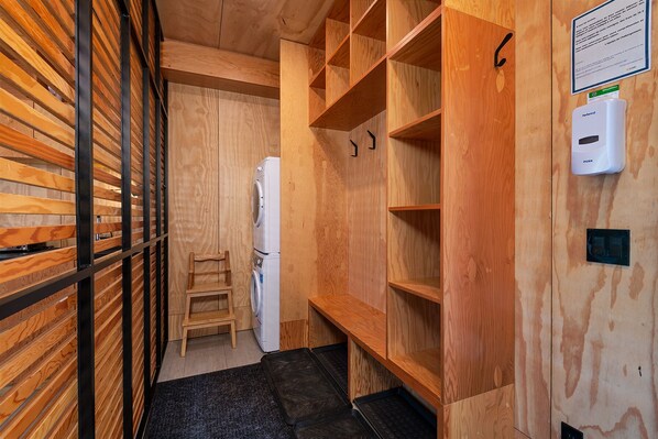 A compact laundry room with a washing machine, wooden shelves, and a small step stool. - Les Refuges (Petite-Riviere-Saint-Francois)