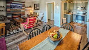 A cozy living room with a fireplace, a dining area with a wooden table and chairs, and a kitchen with modern appliances.