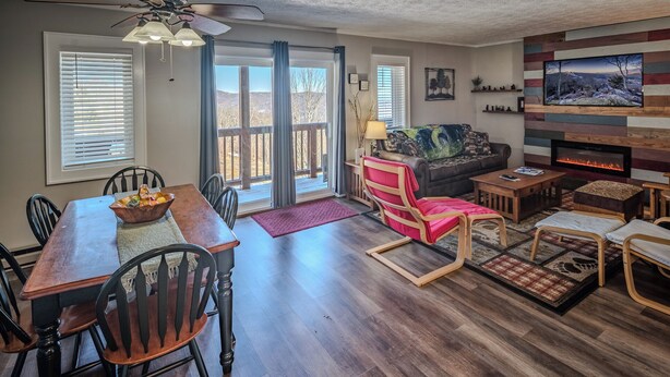 A spacious living room with a fireplace, a dining area with a wooden table and chairs, and a cozy seating area with a red chair and ottoman.