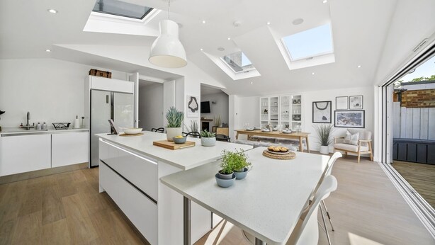 A modern kitchen with skylights, a dining area with a white table, and a view of the outdoors.