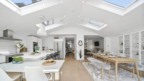 A modern kitchen with skylights, a dining area with a bench, and a living space with a TV and shelves.