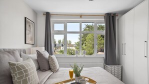 A bedroom with a large window, a bed with grey bedding, a tray with breakfast, and a radiator below the window.