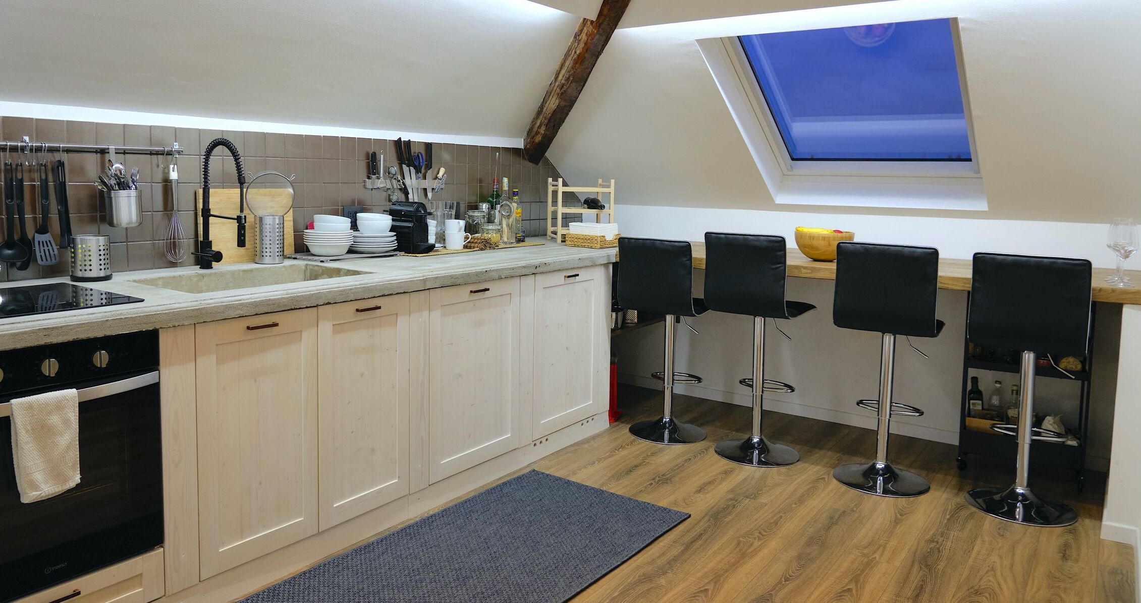 A modern kitchen with a skylight, wooden cabinets, a black stove, and bar stools.