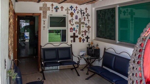 Een kamer met twee blauwe banken, een tafeltje met een speaker, en een muur versierd met verschillende kruisen.