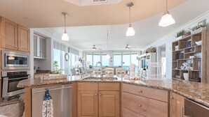 Une cuisine spacieuse dotée de plans de travail en granit, d’armoires en bois, d’appareils électroménagers en acier inoxydable et de luminaires suspendus.