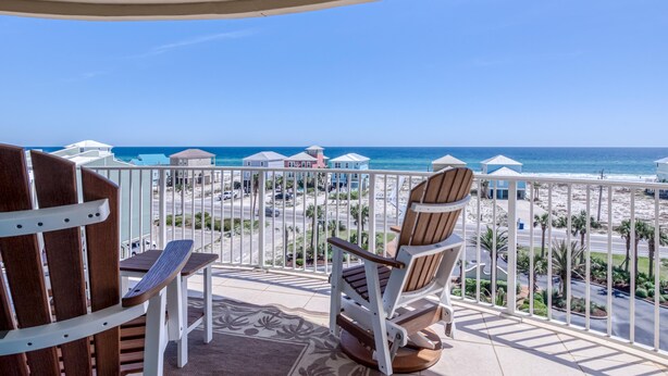 Un balcon avec deux chaises en bois et une table, donnant sur une plage et l’océan.