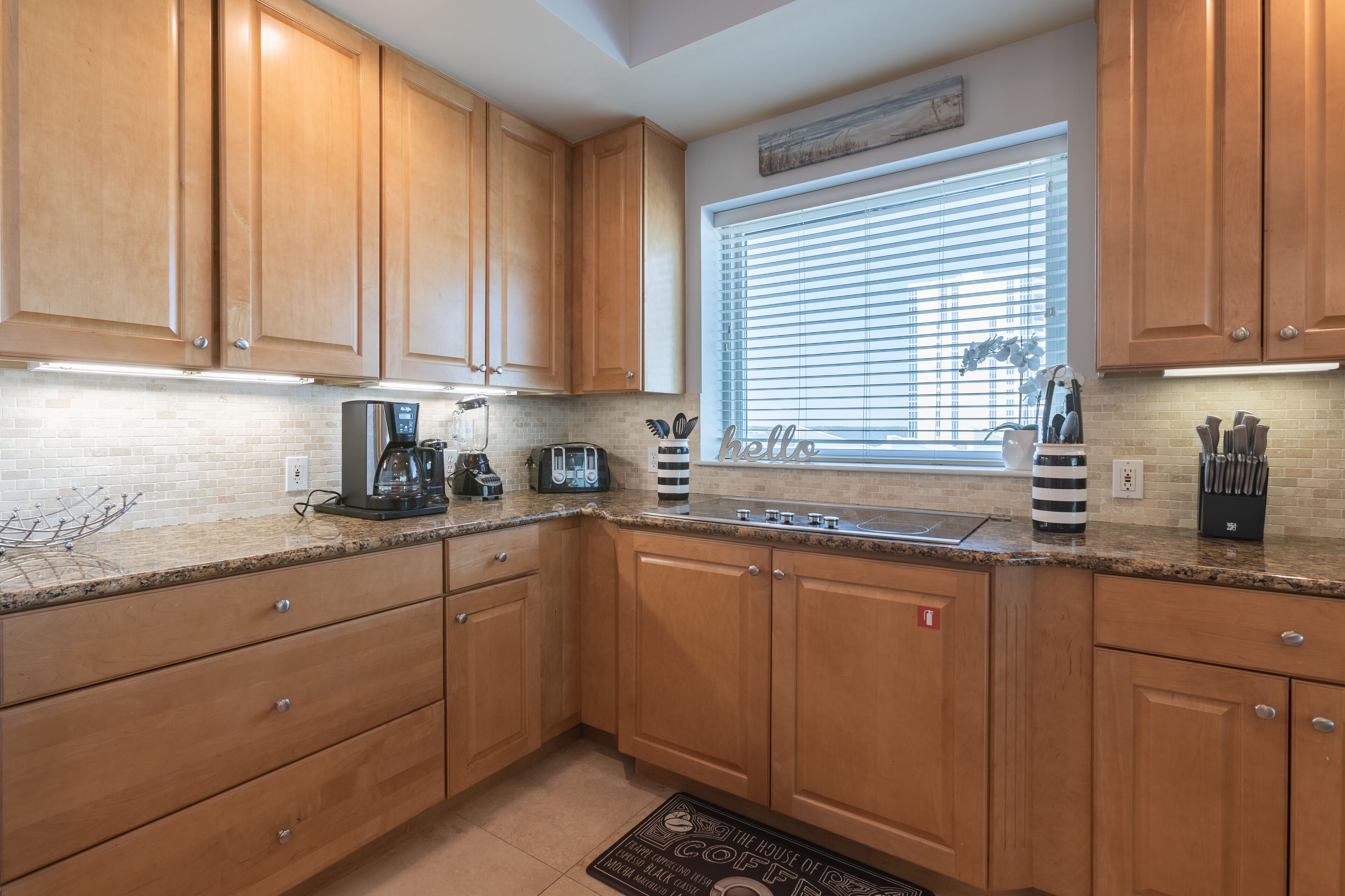 A kitchen with wooden cabinets, a granite countertop, a coffee maker, and a window with blinds.