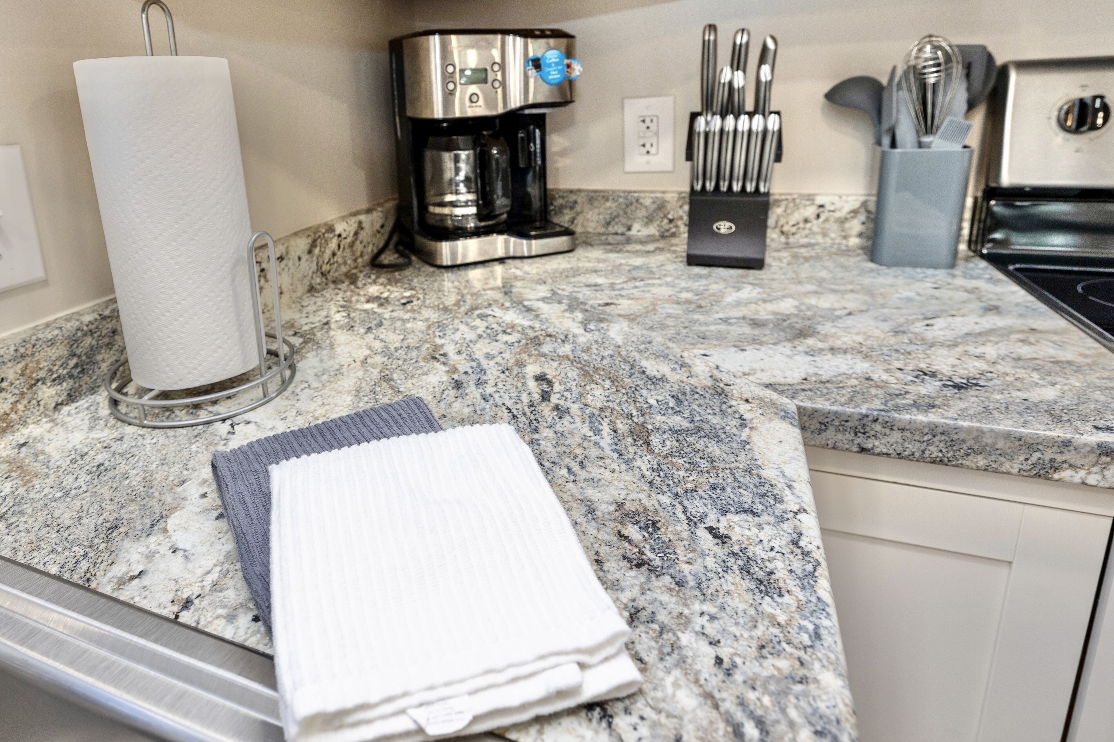 A kitchen with a coffee maker, paper towel holder, and utensils on a granite countertop.