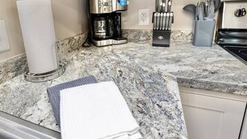 A kitchen with a coffee maker, paper towel holder, and utensils on a granite countertop.