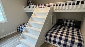 A room with a bunk bed, a white staircase, and a white carpet.