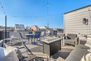 A rooftop patio with outdoor furniture, a fire pit, and string lights.
