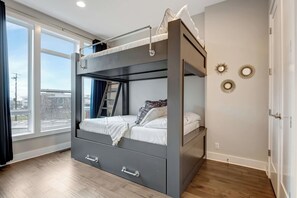 Una cama en literas con una escalera, una ventana con cortinas y vistas a la ciudad.