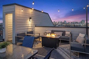 Una terraza en la azotea con mobiliario exterior, una chimenea y vistas al horizonte de la ciudad.