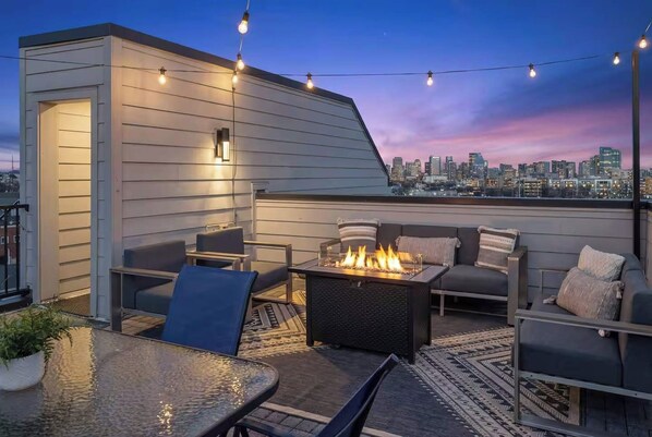 Una terraza en la azotea con mobiliario exterior, una chimenea y vistas al horizonte de la ciudad.