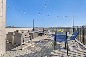 Una terraza en la azotea con mobiliario exterior, luces colgantes y vistas a la ciudad.