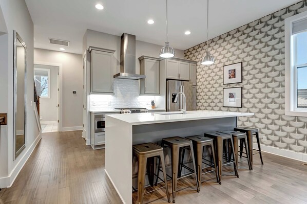 Una cocina moderna con una isla central, taburetes de bar, electrodomésticos de acero inoxidable y un papel tapiz decorativo.