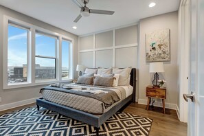 A bedroom with a bed, a ceiling fan, a window, and a nightstand with a lamp.