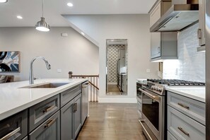 Una cocina moderna con una isla grande, electrodomésticos de acero inoxidable y una escalera que sube a un nivel superior.