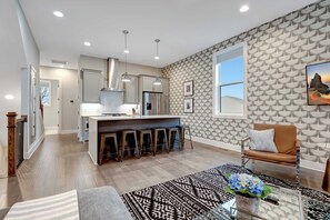 A modern kitchen with a central island, bar stools, pendant lighting, and a patterned wallpaper.