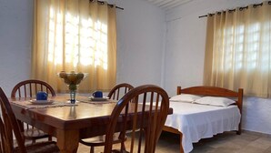 A room with a wooden dining table, four chairs, a bed with white bedding, and two windows with curtains. - Loft das Águas (MG)