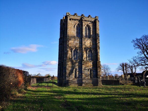 A tall stone tower with arched windows and a gate, surrounded by a grassy field and trees.