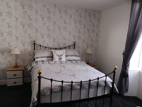 A bedroom with a bed featuring a deer-themed duvet cover, two bedside tables with lamps, and a window with curtains. - The Cambus Flat, Cambuskenneth, Stirling (Stirling)