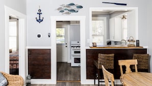 Un comedor con una mesa y sillas de madera, una cocina visible a través de un vano abierto, y un adorno decorativo en la pared.