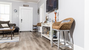 Un salón con sofá, mesa de centro y televisión. Hay sillones de mimbre y una mesita con una vela.