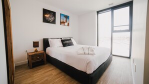 Et moderne hotelværelse med en stor seng, et natbord med lampe og to billeder på væggen.