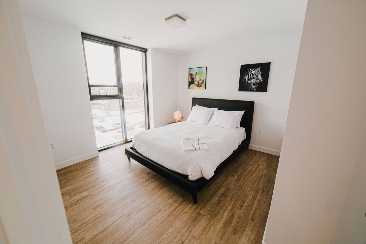 A bedroom with a large bed, a sliding glass door to a balcony, and two framed pictures on the wall.
