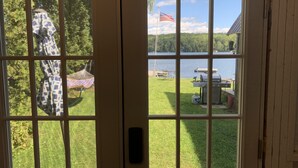 A view through a door with a window, displaying a grassy area with a grill and an American flag, and a hammock. - on gorgeous Great Pond (lake), great for families!  (Belgrade)