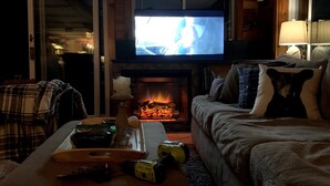 A cozy living room with a fireplace, a television mounted above it, and a couch with decorative pillows. - on gorgeous Great Pond (lake), great for families!  (Belgrade)