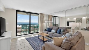 Ein modernes Wohnzimmer mit einem großen Schiebeglasfenster, das auf einen Balkon mit Meerblick führt.