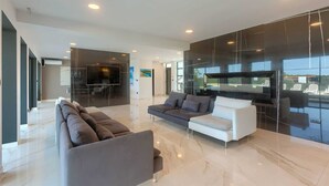 Uma sala de estar moderna com uma televisão de tela grande, um sofá e uma poltrona branca.