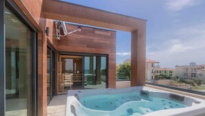Um edifício moderno com entrada por porta de vidro, uma banheira de hidromassagem na varanda e vista para outros edifícios ao fundo.