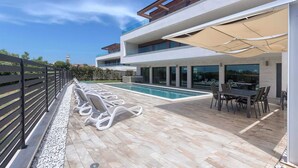 Uma área moderna com piscina ao ar livre, cadeiras de descanso e uma mesa de jantar sob uma pérgula.