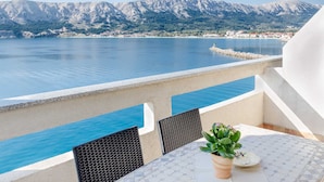 A balcony with a table and chairs overlooking a body of water and a mountainous landscape. - Lori Red - Cozy Hideaway for Two with sea view 🌊 (Baška)