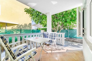 Une terrasse couverte avec une table et des chaises, une rambarde en verre et une vue sur un arbre verdoyant.