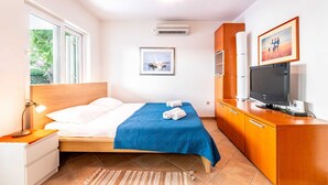 A hotel room with a bed, a TV, a desk, a chair, a lamp, a window, and a picture on the wall. - Ema - Cozy Pet-friendly Suite for Two with Parking (Baška)