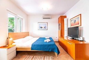 A hotel room with a bed, a TV, a desk, a chair, a lamp, a window, and a picture on the wall.