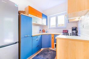 Eine kleine Küche mit Kühlschrank, Schränken, Herd und Fenster.