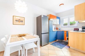 Una cocina compacta con refrigerador, una mesa de comedor con sillas y un ventanal con vistas a la vegetación.