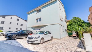 A two-story building with a stone-paved entrance, parked cars, and a tree. - Ema - Cozy Pet-friendly Suite for Two with Parking (Baška)