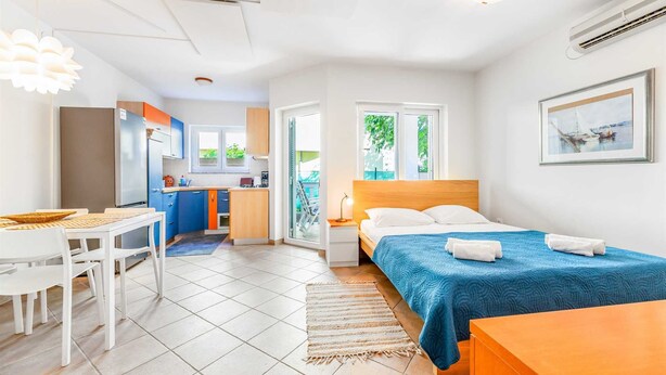 Ett kompakt hotellrum med en säng, ett skrivbord, ett litet kök och utsikt över grönområden.
