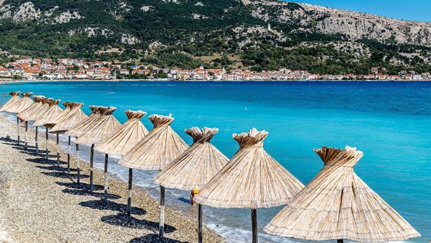 Een strand met strooien parasols en kiezelstenen.