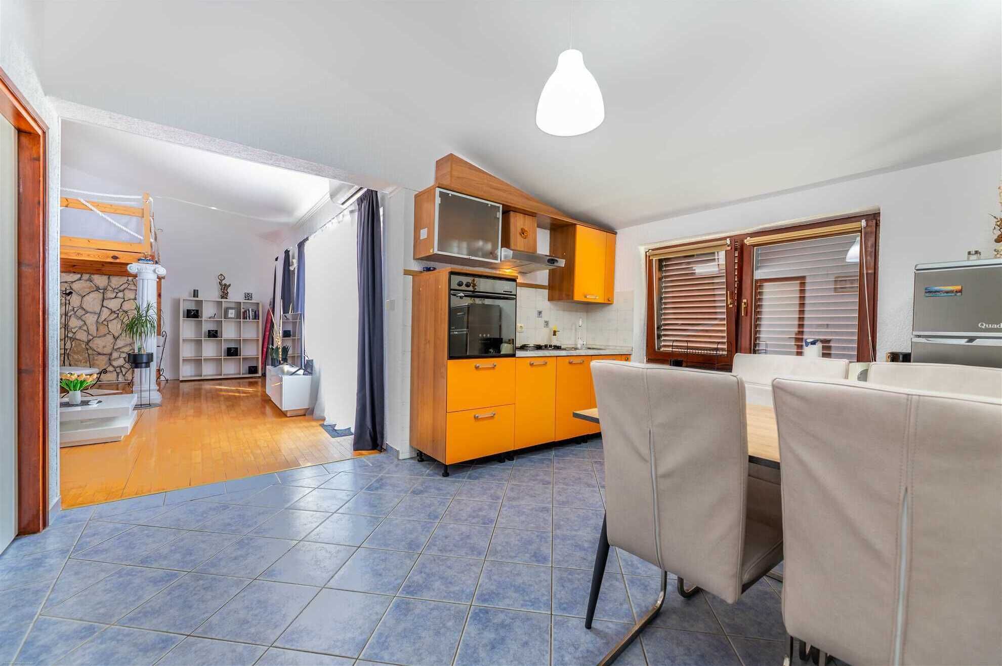 Een compacte keuken met oranje kastjes, een eethoek met tafel en stoelen, en een moderne hanglamp.