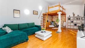Een woonkamer met een groene bank, een witte salontafel, een houten ladder en een stenen muur.