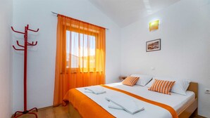 Une chambre d’hôtel avec un lit, des rideaux orange, un porte-manteau et un tableau encadré au mur.