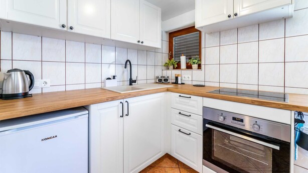 Une cuisine moderne avec des meubles blancs, un plan de travail en bois, un four encastré et une bouilloire.