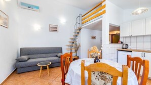 Un espace de vie compact comprenant un canapé, une table à manger, des chaises, un petit coin cuisine et un escalier en bois.